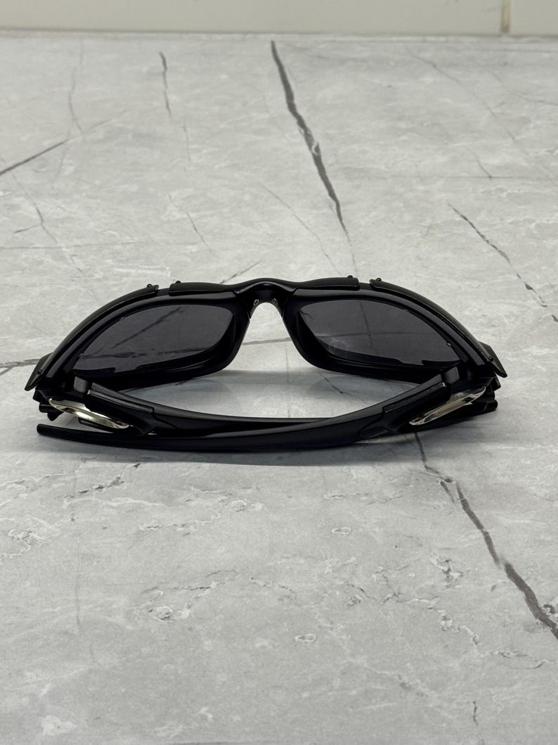 May include: Black sport sunglasses with a curved, wraparound design. The sunglasses have dark lenses and a matte black frame. The arms of the sunglasses are thin and feature silver accents near the hinges. The sunglasses are designed for sports and outdoor activities.