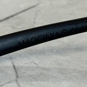 K&ouml;nnte beinhalten: Nahaufnahme eines schwarzen Objekts mit dem gepr&auml;gten Text "MADE IN U.S.A.". Das Objekt scheint Teil eines gr&ouml;&szlig;eren Gegenstands zu sein, m&ouml;glicherweise ein Werkzeug oder Zubeh&ouml;r. Der Hintergrund ist eine helle, strukturierte Oberfl&auml;che.