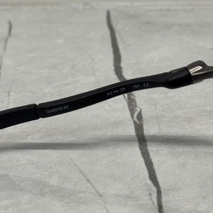 以下が含まれることがあります： フレームに「QO6019-01」、「42-29」、および「151 CE」のテキストが印刷された黒い眼鏡のクローズアップ。 眼鏡は、明るいグレーと白の背景に配置されています。