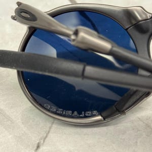 May include: Close-up of a pair of sunglasses with a dark gray frame and blue lenses. The lenses are marked with the word "POLARIZED". The arms of the sunglasses are black and gray.