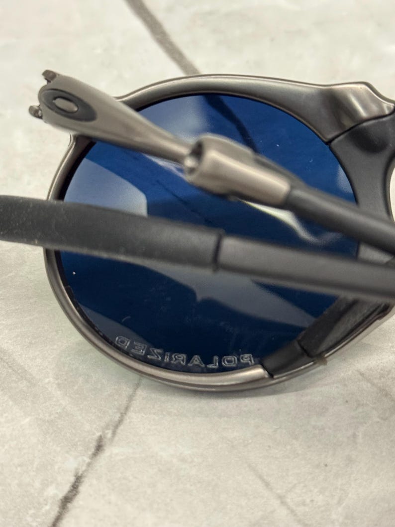 May include: Close-up of a pair of sunglasses with a dark gray frame and blue lenses. The lenses are marked with the word "POLARIZED". The arms of the sunglasses are black and gray.