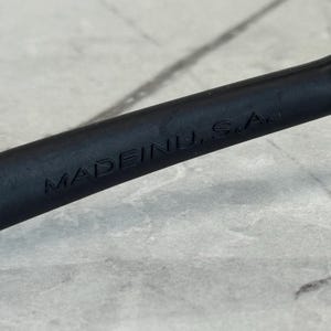 May include: Close-up of a black object with the embossed text "MADE IN U.S.A." The object appears to be a handle or part of a tool, set against a light gray, textured background.