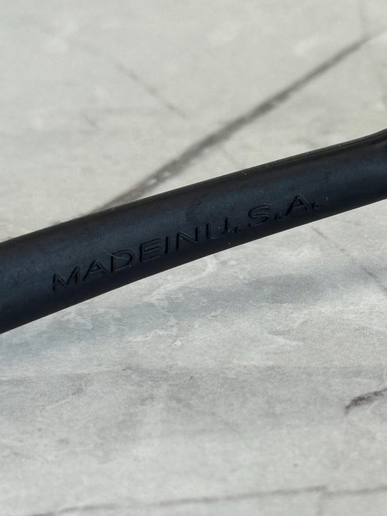 May include: Close-up of a black object with the embossed text "MADE IN U.S.A." The object appears to be a handle or part of a tool, set against a light gray, textured background.