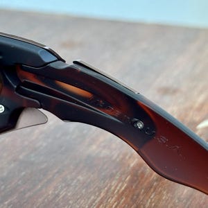 Puede incluir: Primer plano de gafas de sol con un patr&oacute;n de carey marr&oacute;n. El texto "MADE IN U.S.A." es visible en la patilla de las gafas. Las gafas de sol est&aacute;n sobre una superficie de madera marr&oacute;n claro.