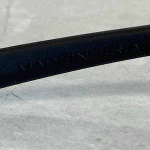 May include: Close-up of a black object with the text "MADE IN U.S.A." embossed on its surface. The object appears to be made of a smooth material, possibly leather or plastic.