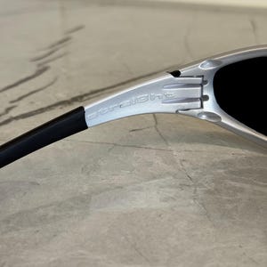 May include: Close-up of silver sunglasses with black lenses. The word "straight" is printed on the silver frame. The sunglasses have a black arm.