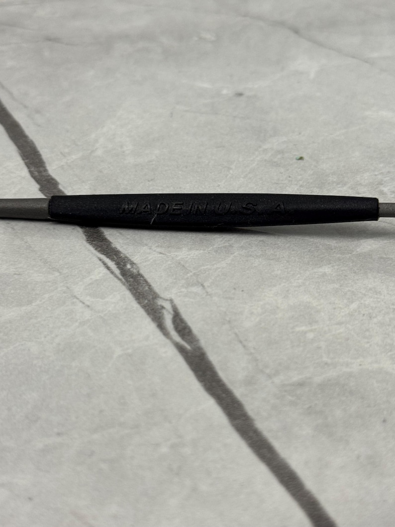 May include: Close-up of a gray and black tool with the text "MADE IN USA" printed on the black section. The tool is set against a light gray, marbled surface.