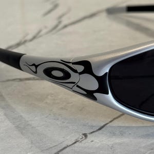 May include: Silver sunglasses with black lenses and a black and white tribal design on the temples. The sunglasses have a sleek, modern design.
