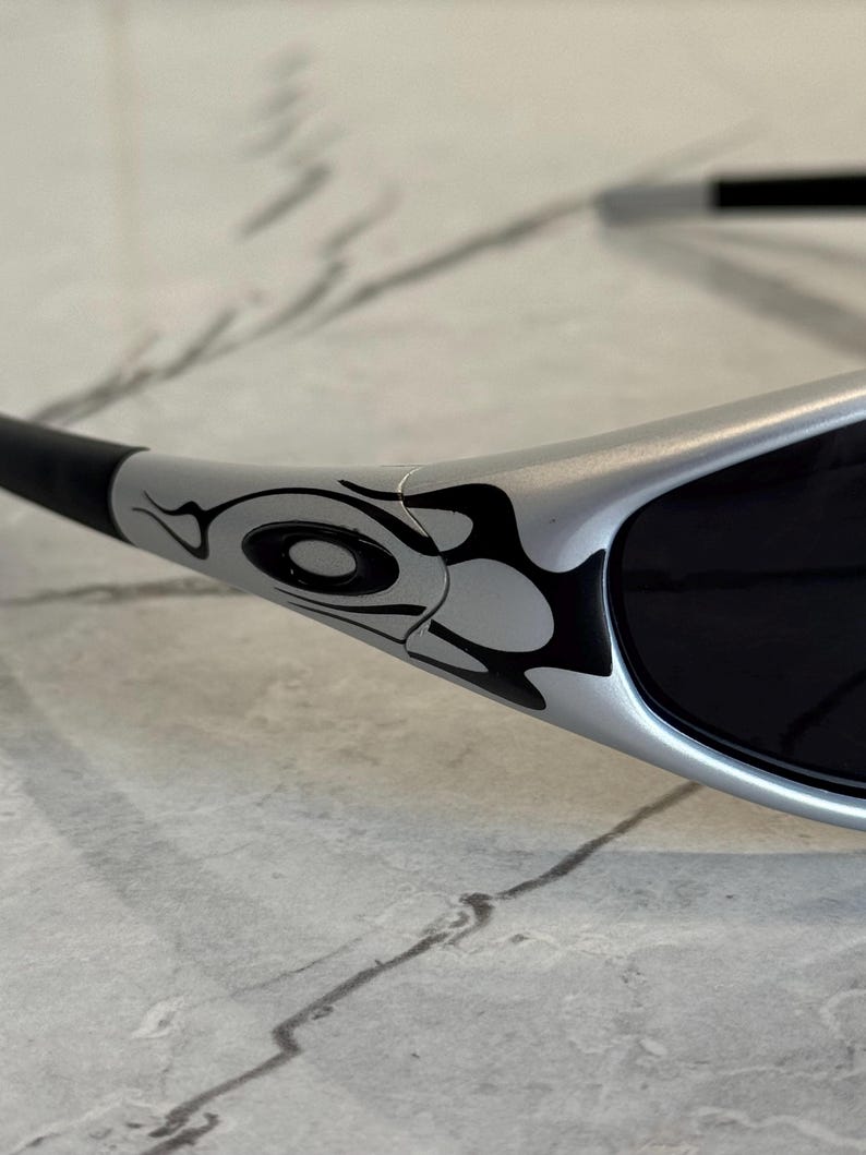 May include: Silver sunglasses with black lenses and a black and white tribal design on the temples. The sunglasses have a sleek, modern design.