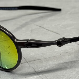 May include: Close-up of a pair of sunglasses with a dark gray frame and yellow-green lenses. The temples are black and extend to the ear. The lenses have a slight curve.