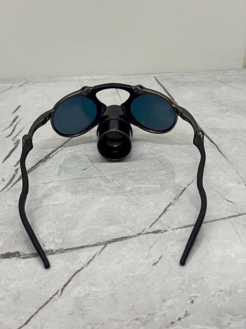 Pu&ograve; includere: Occhiali da sole con montatura nera, lenti blu e un accessorio nero. Gli occhiali da sole hanno un design elegante e moderno. Le lenti sono di un blu vibrante. La montatura &egrave; nera opaca.