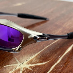 May include: Silver and purple sunglasses with a silver frame and purple lenses. The sunglasses are on a wooden surface.