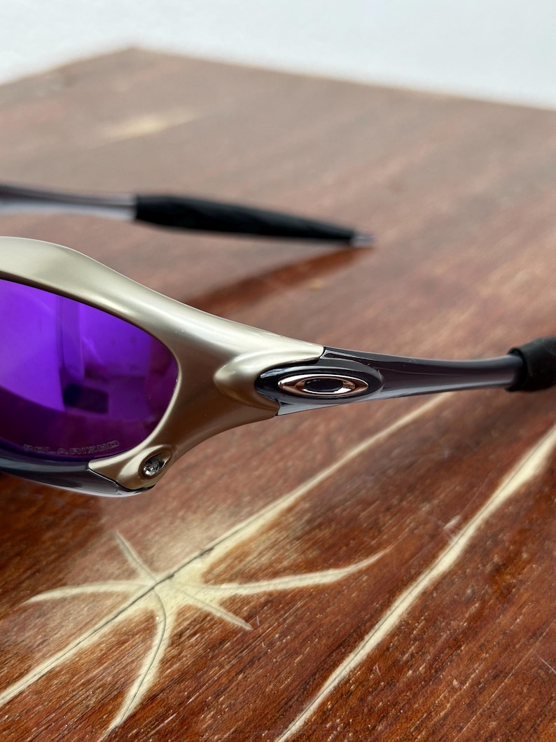 May include: Silver and purple sunglasses with a silver frame and purple lenses. The sunglasses are on a wooden surface.