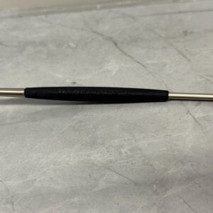 Może przedstawiać: Metalowe narzędzie z czarnym gumowym uchwytem pośrodku. Na czarnym uchwycie wydrukowano napis "MADE IN U.S.A.". Narzędzie ma srebrne wykończenie i jest umieszczone na szarym tle.