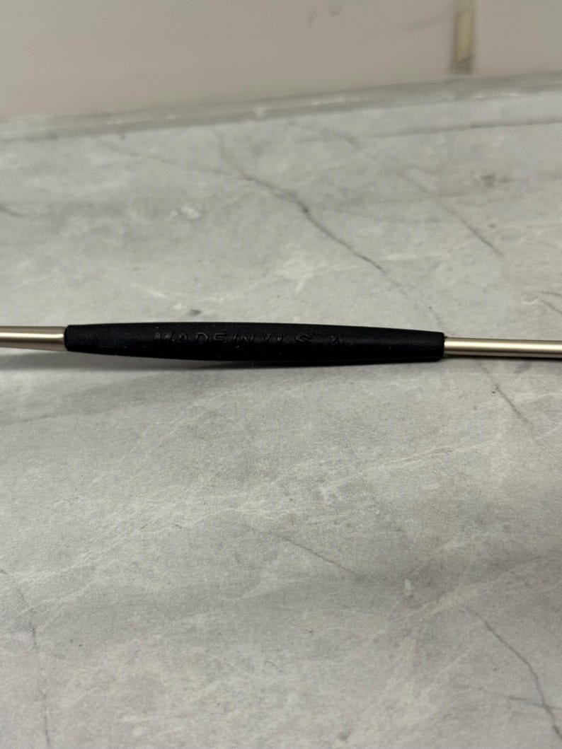 Może przedstawiać: Metalowe narzędzie z czarnym gumowym uchwytem pośrodku. Na czarnym uchwycie wydrukowano napis "MADE IN U.S.A.". Narzędzie ma srebrne wykończenie i jest umieszczone na szarym tle.