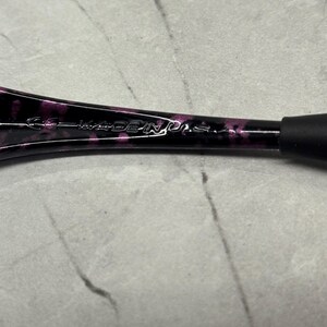 May include: Close-up of a black and purple patterned object with the text "MADE IN U.S.A." The object has a rounded shape and a black rubber grip. The background is a light grey surface.
