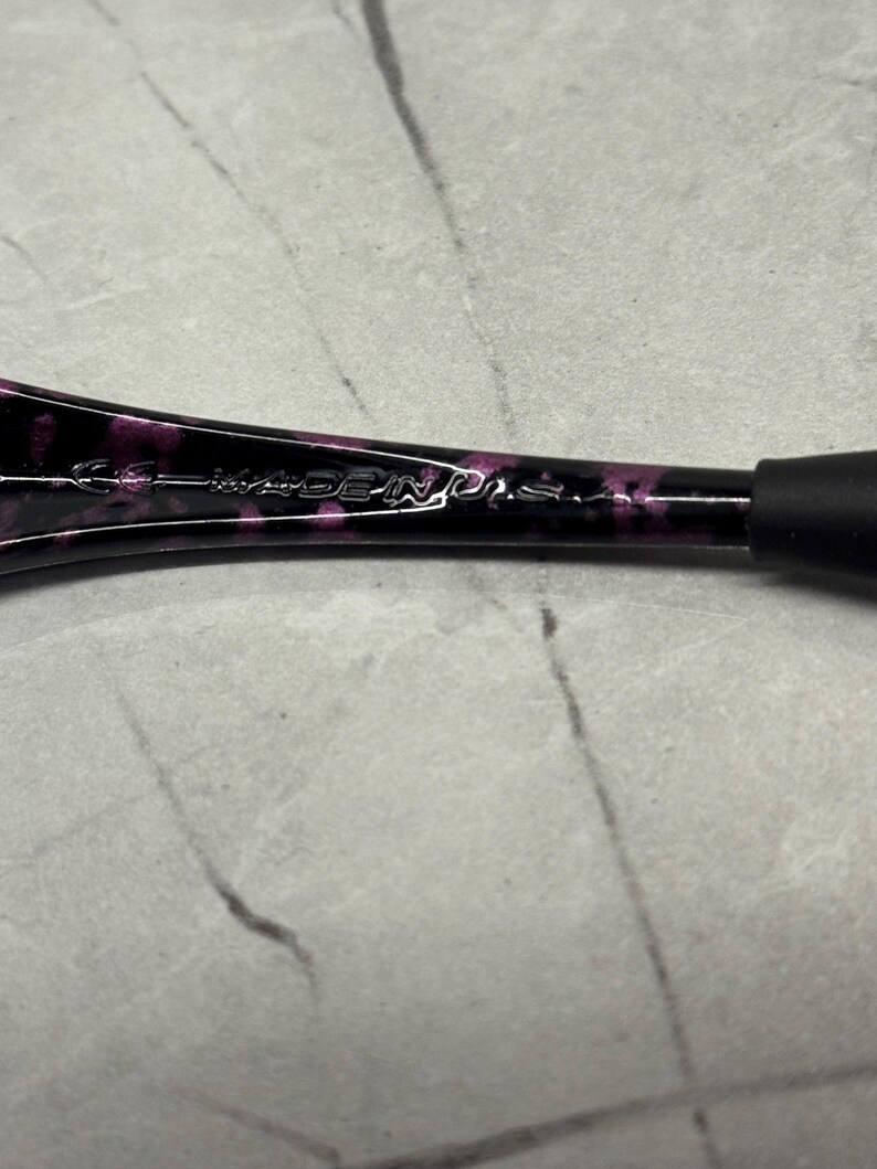 May include: Close-up of a black and purple patterned object with the text "MADE IN U.S.A." The object has a rounded shape and a black rubber grip. The background is a light grey surface.