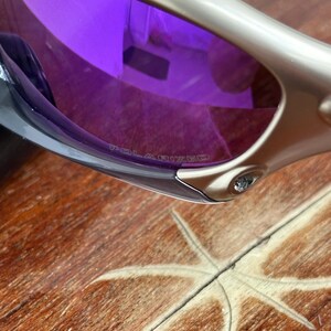 May include: Silver sunglasses with purple polarized lenses. The lenses have the word "POLARIZED" printed on them.