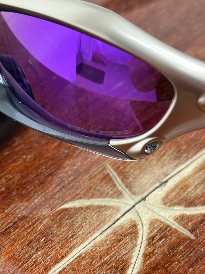 May include: Silver sunglasses with purple polarized lenses. The lenses have the word "POLARIZED" printed on them.