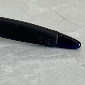 May include: Close-up of a black pen with a dark blue tip. The pen's body is black and has a matte finish. The pen's tip is a glossy dark blue color. The pen is resting on a gray and white marble surface.