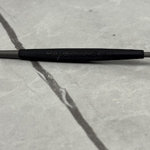 May include: Close-up of a gray and black tool with the text "MADE IN USA" printed on the black section. The tool is set against a light gray, marbled surface.