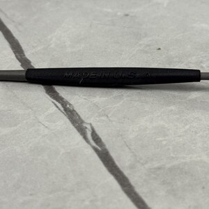 以下が含まれることがあります： 「MADE IN USA」の文字が黒い部分に印刷された、グレーと黒の工具のクローズアップ。明るいグレーの大理石模様の表面に置かれています。