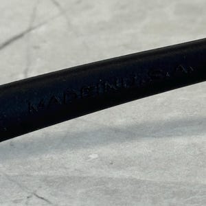 May include: Close-up of a black object with the text "MADE IN U.S.A." embossed on its surface. The object is set against a light grey background.