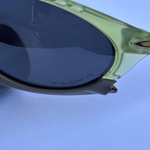 May include: Close-up of a pair of sunglasses with a light green frame and dark lenses. The text "PRIZM" is visible on the lens. The sunglasses have a sleek, modern design.