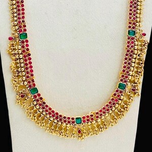 Puede incluir: Un collar de oro con piedras rojas y verdes. El collar tiene un diseño de borla y está hecho de pequeñas cuentas.