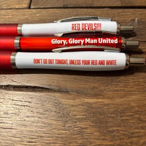 May include: Three red and white pens with silver accents. The pens have text that reads "RED DEVILS!!!", "Glory, Glory Man United", and "DON'T GO OUT TONIGHT, UNLESS YOUR RED AND WHITE".