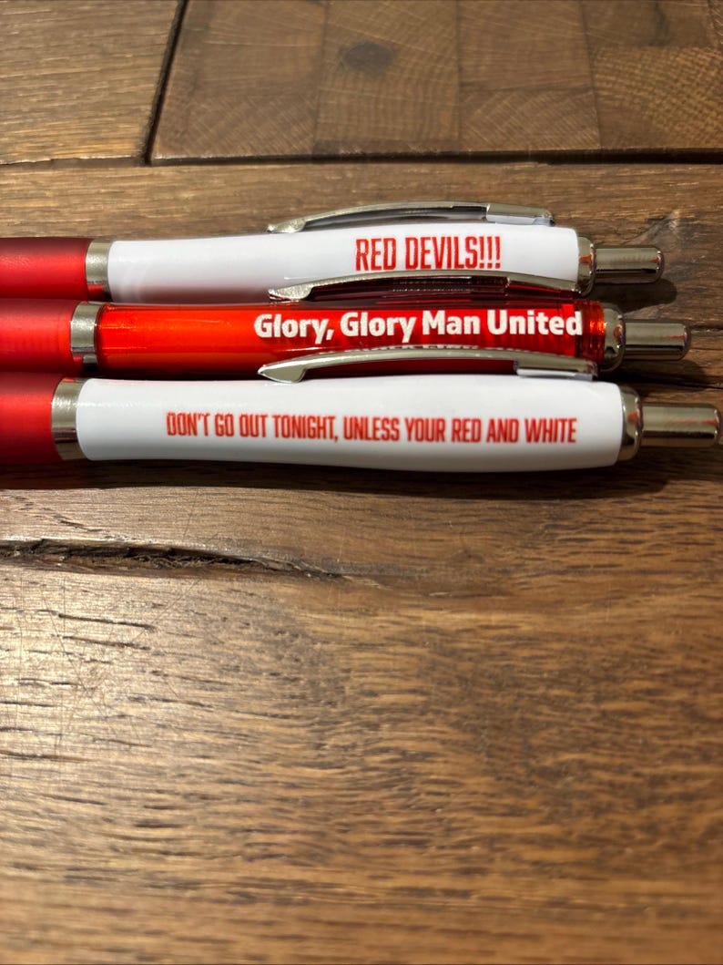 May include: Three red and white pens with silver accents. The pens have text that reads "RED DEVILS!!!", "Glory, Glory Man United", and "DON'T GO OUT TONIGHT, UNLESS YOUR RED AND WHITE".