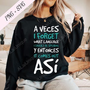 May include: Black sweatshirt with white and teal text that reads "A Veces I Forget What Language I Should Be Speaking Y Entonces It Comes Out Así". The design includes the text "PNG + SVG" in the upper left corner.