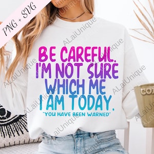 Op de afbeelding: Witte sweatshirt met de tekst "BE CAREFUL. I'M NOT SURE WHICH ME I AM TODAY. YOU HAVE BEEN WARNED" in roze, paars en blauw. Een casual, comfortabele stijl.