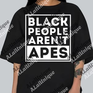 May include: Black t-shirt with a white square containing the text "BLACK PEOPLE AREN'T APES" in a bold, sans-serif font. The shirt is a solid black color and has short sleeves.