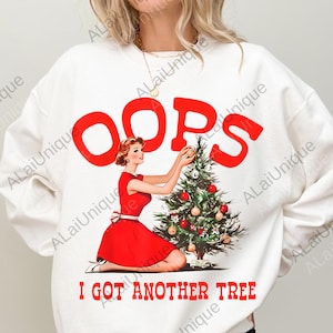 May include: White sweatshirt with a retro design featuring a woman in a red dress decorating a Christmas tree. Bold red text reads "OOPS" above and "I GOT ANOTHER TREE" below, creating a festive and humorous holiday theme.