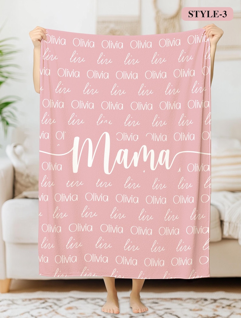 May include: A pink fleece blanket with the word "Mama" written in white cursive script. The blanket is covered in the name "Olivia" written in white script.