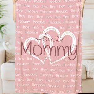 May include: Pink fleece blanket with a white heart design that says "love mommy" and a repeating pattern of the name "Theodore" in a smaller font.
