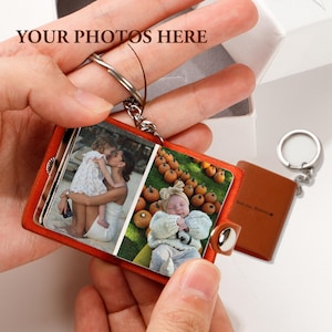 May include: A brown leather photo album keychain with two photo slots. The keychain features a silver metal ring and a silver metal clasp. The photos in the album show a woman holding a young girl and a baby sleeping in a pumpkin patch.