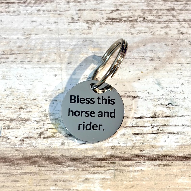以下が含まれることがあります： Bless this horse and riderという黒い刻印が施された、光沢のある反射面を持つ円形の銀色金属タグ。タグの上部には穴が開いており、小さな金属製の二重リングが取り付けられています。
