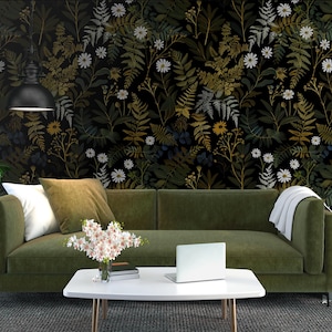 May include: A living room scene featuring a green sofa with white and olive-green pillows, a white coffee table with a laptop, and a floral wallpaper backdrop. A potted plant and a small side table with a lamp are also visible.
