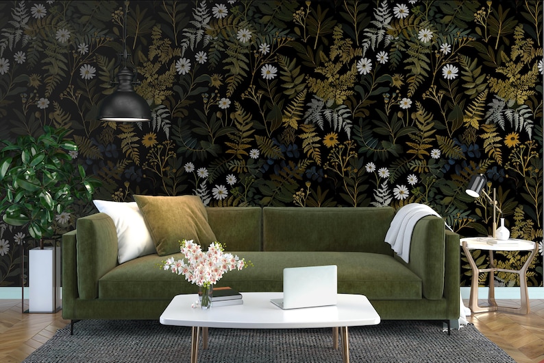 May include: A living room scene featuring a green sofa with white and olive-green pillows, a white coffee table with a laptop, and a floral wallpaper backdrop. A potted plant and a small side table with a lamp are also visible.