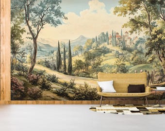 Op de afbeelding: Een muurschildering van een Europees landschap met heuvels, bomen en een villa. Voor de muurschildering staat een gele rotan bank met witte en bruine kussens. Een kleine bijzettafel en een patroonkleed maken de scène compleet.