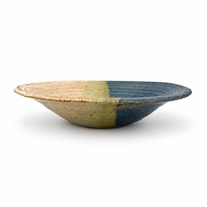 May include: A shallow ceramic bowl featuring a tri-color design with a speckled beige section, a muted olive green center band, and a deep blue side. The surface of the bowl is textured with concentric circular grooves along the wide rim.