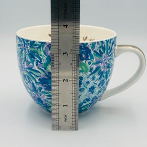 May include: A ceramic mug with a white handle and gold trim. The mug features a blue, green, and purple floral pattern. The mug is approximately 4 inches tall.