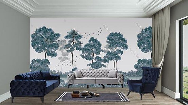 May include: A contemporary living room with a mural depicting trees in blue and grey tones. The room is furnished with a navy blue sofa, a grey tufted sofa, and a navy blue armchair. A dark rug and books are also present.
