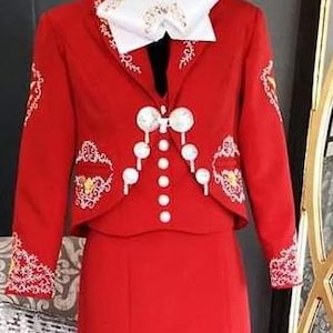 May include: A red charro suit with white embroidery and pearl-like buttons. The suit includes a jacket, a vest, and a skirt.