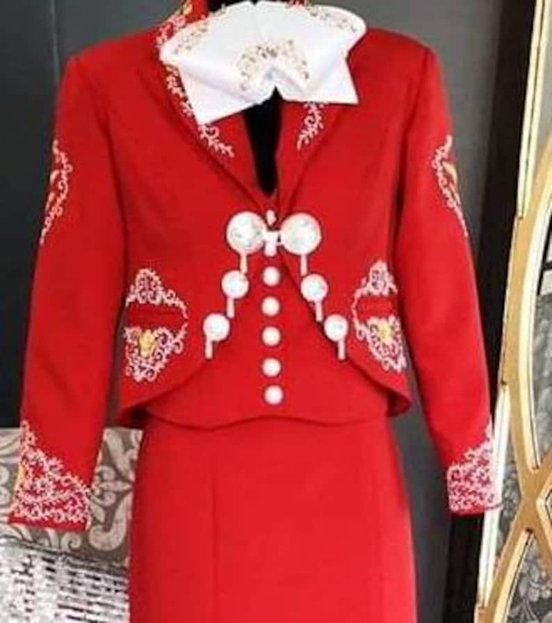May include: A red charro suit with white embroidery and pearl-like buttons. The suit includes a jacket, a vest, and a skirt.
