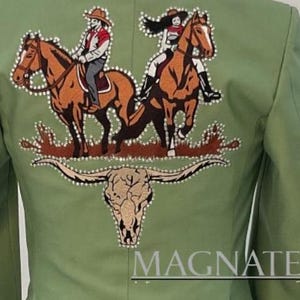 May include: Sage green jacket with an embroidered design featuring two riders on horseback, a steer skull, and the word "MAGNATE". The design is embellished with rhinestones. The jacket has a tailored fit.