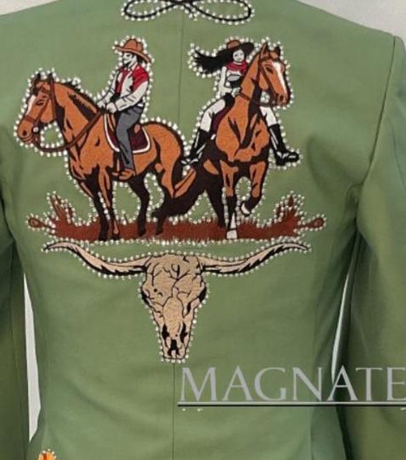 May include: Sage green jacket with an embroidered design featuring two riders on horseback, a steer skull, and the word "MAGNATE". The design is embellished with rhinestones. The jacket has a tailored fit.
