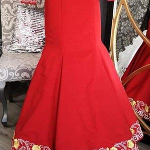 May include: A red mermaid-style skirt with gold and white embroidery around the hem. The skirt is made of a smooth fabric and has a fitted waist.